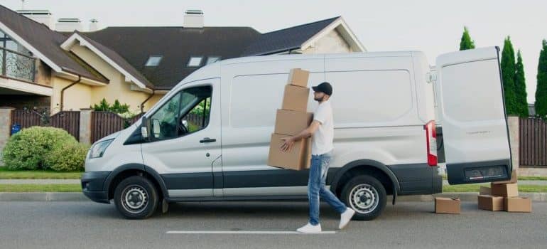 A mover carries boxes next to a van